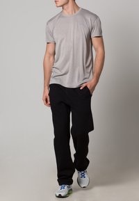 Ljust grå träningströja med korta ärmar, ihopparad med svarta joggingsbyxor och vita sneakers med blå detaljer.