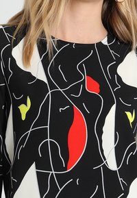 Mustapuku, jossa on abstrakteja viivapiirroksia valkoisena, punaisena ja keltaisena, muotoillulla siluetilla ja pyöreällä kaula-aukolla. Silkkinen kankaan rakenne.