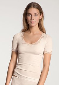 Beige kortarmpige top met geribbelde textuur, voorzien van een gegolfde kant-halssnit en mouwranden. De pasvorm is aansluitend en soepel.