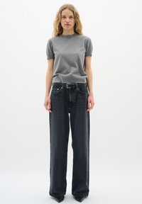 Grau kurzärmliger Pullover kombiniert mit taillenhohen, weit geschnittenen schwarzen Jeans aus Denim. Das Outfit wird durch einen schwarzen Gürtel und spitze Schuhe ergänzt.