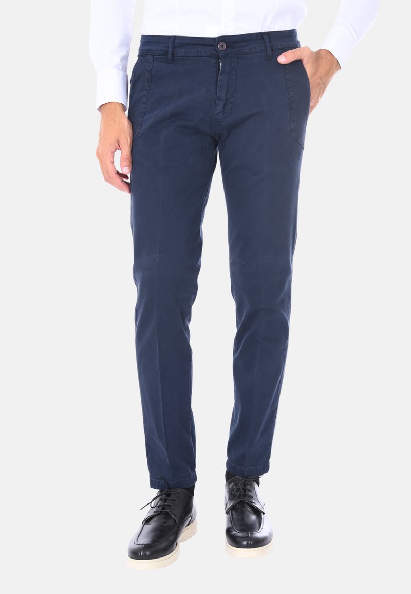 Pantaloni in cotone blu navy con vestibilità slim, dotati di vita con bottone, tasche laterali e una texture liscia. Abbinati a scarpe in pelle nera.