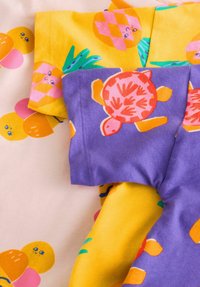Färgglada barntröjor: en med tryck av ananas och apelsin, en annan med sköldpaddedesign på lila bakgrund och i bomullsmaterial.