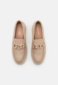 Beige suede loafers med gullkjede aksent, rund tå og teksturert såle. Innvendig har de myk fôr med merkevaren sitt logo.