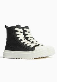 Wysokie trampki z czarnego płótna z kremowymi sznurowadłami, białą gumową podeszwą i teksturowanym wykończeniem, z okrągłym noskiem i wzmocnionym przeszyciem.