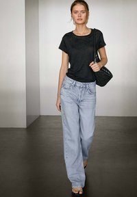 Zwarte korte mouwen t-shirt met een ronde hals, gecombineerd met lichtblauwe wijde jeans. Het model draagt een geweven zwarte handtas.
