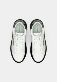 Adidași albi cu o parte superioară din piele netedă, talpă din cauciuc negru și închidere cu șireturi. Caracteristicile includ un toc translucid contrastant și detalii de branding.