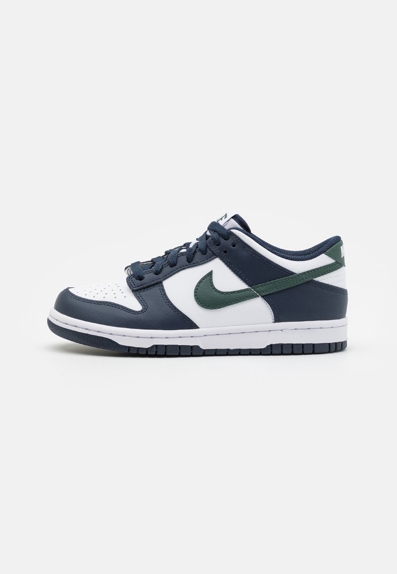Baskets basses avec base blanche, surpiqûres bleu foncé, logo Nike vert foncé et lacets bleu foncé sur fond blanc.