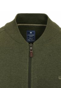 Zielona oliwkowa bluza rozpinana z prążkowanym kołnierzem, z dyskretnym brązowym uchwytem do zamka błyskawicznego ze skóry i metką z nazwą marki w środku.