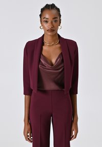 Burgunderfarbenes Dreiteiler-Anzugset mit einem taillierten Blazer, einem satinartigen Top mit cowl Ausschnitt und maßgeschneiderten Hosen; glatte Textur und figurbetontes Design.