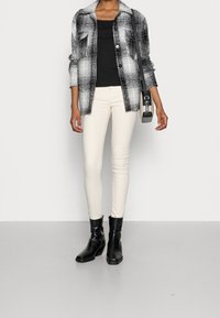 Svartvitt rutigt skjorta, svart linne, krämfärgade tight jeans och svarta ankelstövlar. Skjortan har två bröstfickor och knappstängning.