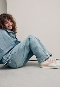 Lyseblå denimjakke kombineret med løstsiddende lyseblå jeans, ledsaget af hvide sneakers med pink detaljer og strukturerede snørebånd.