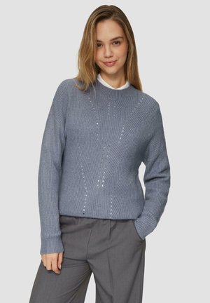 Pull en maille bleu clair avec un col rond, présentant des motifs texturés et de petites embellissements, associé à un pantalon gris.