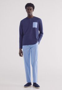 Mariene lange mouw shirt met een lichtblauwe gestreepte patch pocket, gecombineerd met lichtblauwe gestreepte broek en mariene instap schoenen.