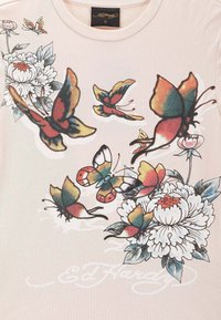 Camiseta rosa claro con estampados gráficos de flores y mariposas en colores vibrantes. Presenta un cuello redondo y una tela suave y lisa.
