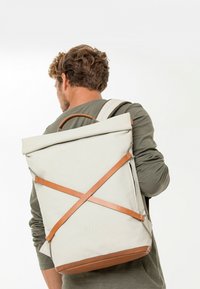 Zaino roll-top in tessuto beige chiaro con dettagli in pelle. Presenta spallacci regolabili, una maniglia superiore e una superficie liscia e durevole.