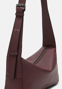 Ciemnogranatowa skórzana torebka na ramię z regulowanym paskiem i górnym zamkiem błyskawicznym na jednolitym tle.