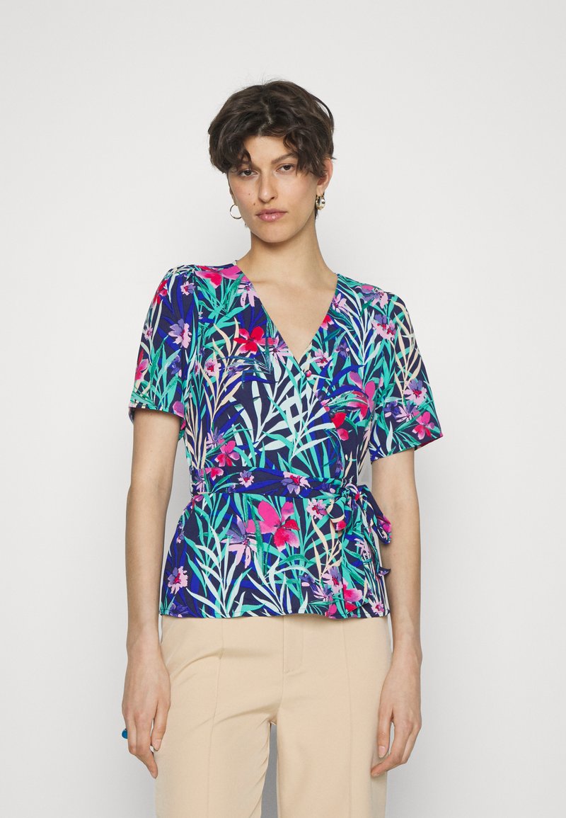 Blusa floral envolvente com decote em V profundo, mangas curtas e cintura com laço. As cores dominantes incluem azul marinho, rosa, verde e branco.