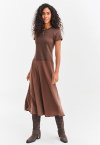 Brązowa sukienka z krótkim rękawem, dopasowanym górnym partem i rozkloszowanym dołem. Długość do połowy łydki. Połączona z szarymi, wysokimi do kolan, na obcasie kozakami. Gładka faktura.