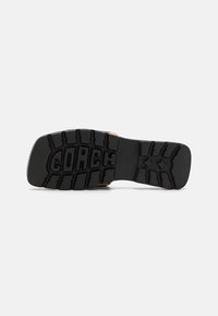 Black rubber sole with textured grip patterns and "COACH" logo. Light brown upper edge visible, showcasing a smooth finish.