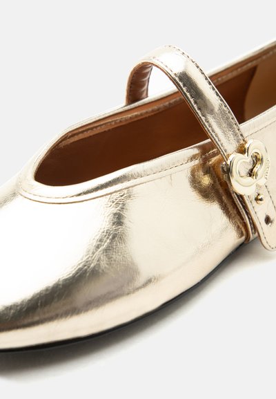 Chaussure plate Mary Jane dorée avec boucle métallique en forme de cœur et bout arrondi sur fond blanc.