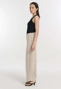 Zwarte tanktop, beige wijde broek met elastische tailleband, en zwarte hoge hakken. Gladde stof met een relaxed fit.