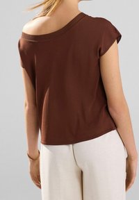 Brun, løstsiddende top med rullede korte ærmer og off-shoulder halsudskæring, parret med lyse, vide bukser. Glat tekstur.