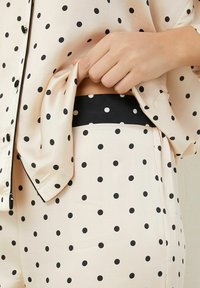 Pajama set featuring a light pink fabric with black polka dots, a button-up shirt, and black elastic waistband on the pants.