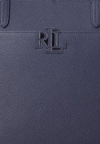 Mornarsko modra usnjena torba z teksturirano površino in vtisnjenim logotipom "RL" na sredini. Gladki, trdni ročaji dopolnjujejo oblikovanje.