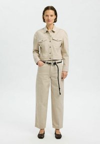 Chaqueta de mezclilla beige con bolsillos frontales, combinada con pantalones beiges de cintura alta y cinturón trenzado negro, accessorisada con bailarinas de malla negras.