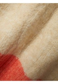 Stickad tyg som visar en mjuk, beige textur med en slät, luddig yta, med en djärv orange färgblock på en kant.