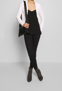 Svart spetstopp under en vit blazer, kombinerat med svarta skinnybyxor. Grå snakeskinmönstrade ankle boots och en svart crossbody-väska ger detaljer.