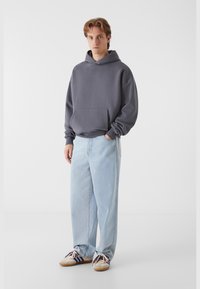 Grå bomulds hoodie med en frontlomme, parret med lyseblå loose-fit jeans og beige sneakers med blå striber. Minimalistisk design.