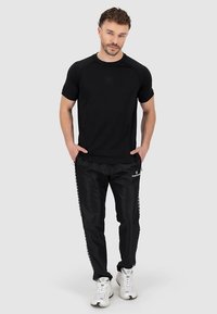 Zwart T-shirt met korte raglanmouwen, gecombineerd met zwarte trainingsbroeken met logo's aan de zijkant. Beide items hebben een gladde textuur.