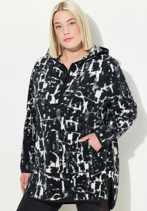 Pull en polaire noir et blanc avec un motif abstrait, présentant un col zippé demi-fermeture, des poches latérales et une coupe légèrement allongée.
