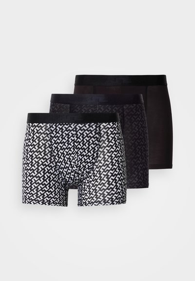 Três pares de boxers masculinos: um com padrão geométrico em preto e branco, dois pretos sólidos com cinturas elásticas. Tecido macio, design respirável.
