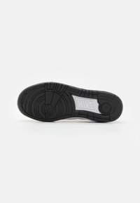Sola de sapatilha Nike com um acabamento em borracha preta texturizada, apresentando um padrão de design circular e um logótipo Nike branco embutido na entressola.