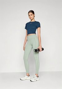 Sinine lühendatud sportlik särk, helerohelised kõrge vöökohaga retuusid, hoiab käes musta veepudelit, valgete tossudega kombineeritud. Sile kanga tekstuur.