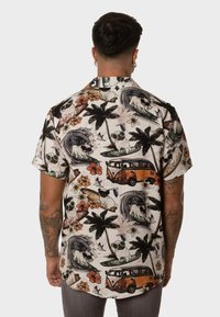 Camisa de manga corta con un fondo claro, que presenta patrones tropicales, palmeras, tablas de surf y una furgoneta vintage naranja. Material de algodón.