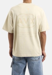 Jasno beżowy, oversize'owy t-shirt z krótkimi rękawami, z nadrukiem na plecach, w tym logo, tekstem i grafiką globu.