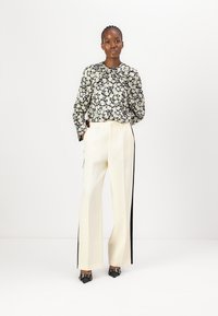 Blusa a maniche lunghe bianca e nera a fantasia floreale abbinata a pantaloni larghi color crema con strisce laterali nere. Scarpe nere a punta.