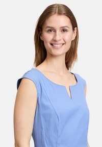 Helles blaues, kurzärmeliges Kleid mit einem runden Ausschnitt und Schlitzdetail. Glatter Stoff mit feiner Textur und einer figurbetonten Silhouette.