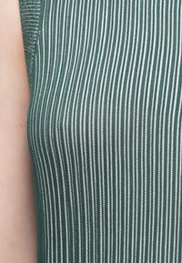 Tecido verde canelado com finas riscas brancas, apresentando uma textura suave e um corte justo. Sem detalhes adicionais visíveis.