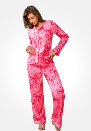 Różowy satynowy komplet piżamowy z nadrukiem kokardek i serc, z długimi rękawami, zapinana na guziki koszula oraz luźne spodnie.