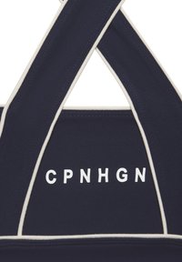 Tumesinine spordirinnahoidja kreemja äärega, millel on ristis rihmad ja julge valge kiri "CPNHGN" ees. Sile kangatunne.