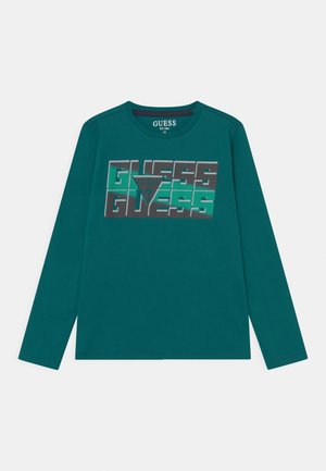 Maglia a maniche lunghe color teal con testo "GUESS" sovrapposto e logo a triangolo al centro, taglia 10, collo a girocollo.