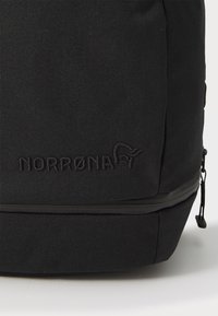Čierny látkový batoh s textúrovaným povrchom, so zipsovým oddelením a embosovaným logom "NORRØNA" na prednej strane.