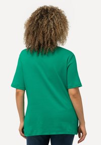 Grøn t-shirt med korte ærmer lavet af glat stof med en afslappet pasform, der har en rund halsudskæring og et længere bagstykke.