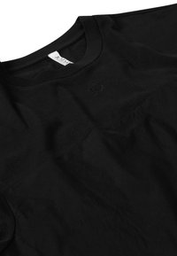 Camiseta negra con cuello redondo, logo bordado sutil en el pecho y una combinación de paneles de tela lisa y texturizada.