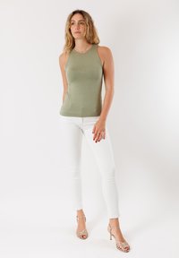 Top senza maniche verde oliva con un design aderente, abbinato a jeans bianchi a taglio slim e tacchi strappy dorati. Texture liscia, dettagli minimi.