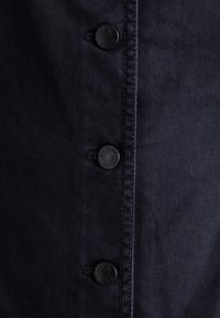 Tissu en denim foncé présentant une rangée de quatre boutons noirs sur le devant, avec une couture subtile et une texture lisse.